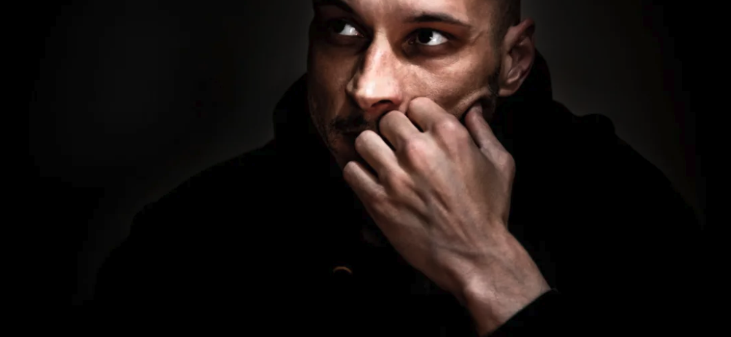 man looking off into the distance in a dark room thinking